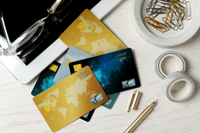 Different credit cards, tablet and stationery on white wooden table, flat lay