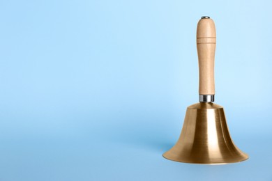 Golden school bell with wooden handle on light blue background. Space for text
