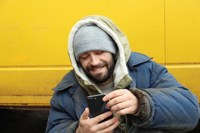 Poor homeless man with stolen smartphone outdoors