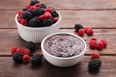 Photo of Blackberry puree in bowl and fresh berries on wooden table