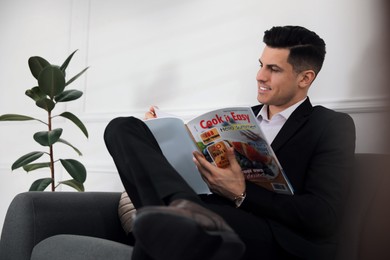 Photo of Man reading new magazine on sofa indoors