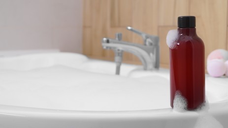 Red bottle of bubble bath on tub indoors, space for text