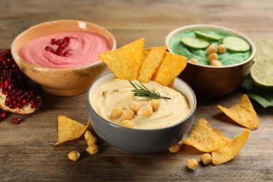 Different kinds of tasty hummus, nachos and ingredients on wooden table
