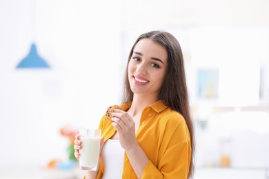 Beautiful young woman drinking milk with cookies at home