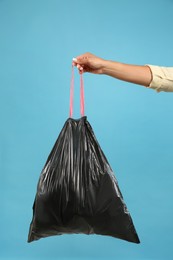 Woman holding full garbage bag on light blue background, closeup