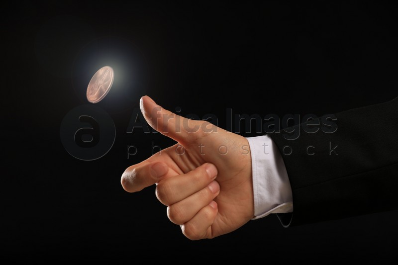 Man throwing coin on black background, closeup. Making decision
