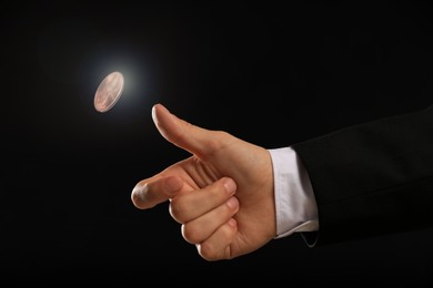 Man throwing coin on black background, closeup. Making decision
