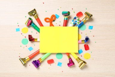Flat lay composition with party blowers and blank card on wooden background. Space for text