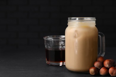 Photo of Mason jar of delicious iced coffee, syrup and hazelnuts on black table. Space for text