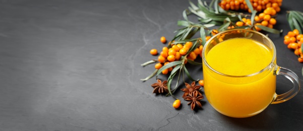 Sea buckthorn tea and fresh berries on grey table, space for text. Banner design
