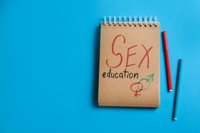 Notebook with phrase "SEX EDUCATION" and gender symbols on blue background, flat lay. Space for text