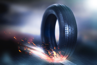 Car tire with flame rolling on road against blurred background