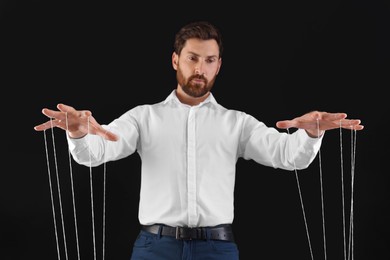 Photo of Man in formal outfit pulling strings of puppet on black background, low angle view