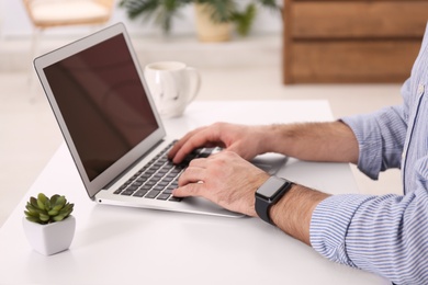 Young man with smart watch working on laptop at table in office, closeup