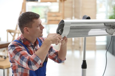 Professional technician repairing electric infrared heater with pliers indoors