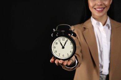 Businesswoman holding alarm clock on black background, closeup with space for text. Time management
