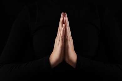 Woman holding hands clasped while praying in darkness, closeup
