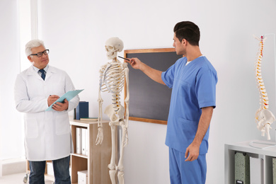 Medical student and professor studying human skeleton anatomy in classroom