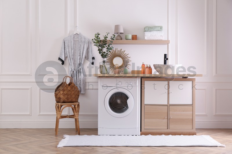 Photo of Laundry room interior with modern washing machine and stylish vessel sink on countertop