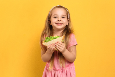 Photo of Cute little girl with tasty sandwich on yellow background