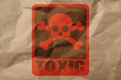 Hazard warning sign (skull-and-crossbones symbol and word TOXIC) on crumpled kraft paper, top view