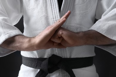 Karate coach wearing kimono and black belt on dark background, closeup