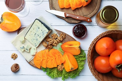 Photo of Delicious persimmon, blue cheese and nuts served on white wooden table, flat lay