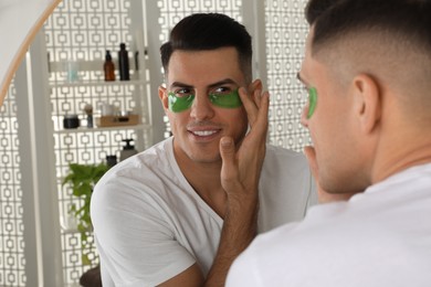 Man applying green under eye patch near mirror at home