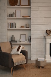Comfortable armchair near shelves with different decor in room. Interior design