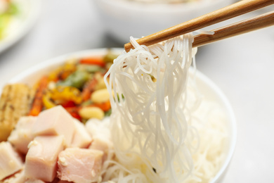 Chopsticks with tasty cooked rice noodles over bowl, closeup