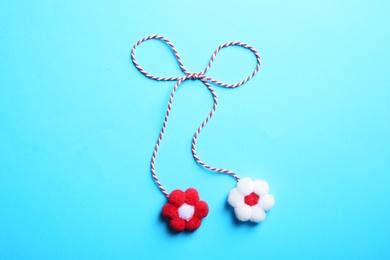 Traditional martisor with flowers on light blue background, top view. Beginning of spring celebration