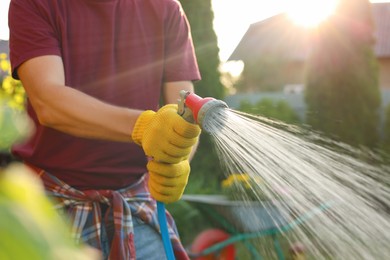 Photo of Man watering plants from hose outdoors on sunny day, closeup. Gardening time