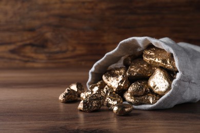 Overturned sack of gold nuggets on wooden table, closeup. Space for text