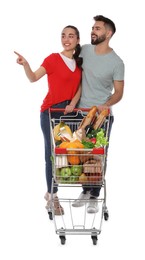 Happy couple with shopping cart full of groceries on white background