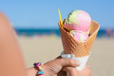 Little girl holding waffle cone with scoops of delicious colorful ice cream at beach on sunny summer day, closeup. Space for text