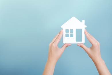Woman holding house model on color background