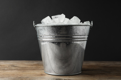 Metal bucket with ice cubes on wooden table