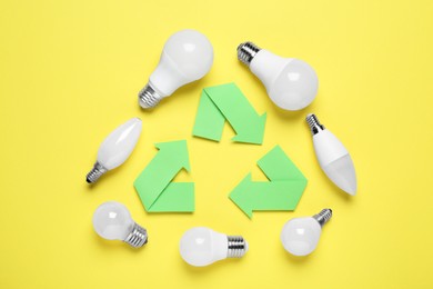 Photo of Recycling symbol and light bulbs on yellow background, flat lay