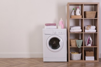 Photo of Laundry room interior with modern washing machine and shelving unit near white wall. Space for text