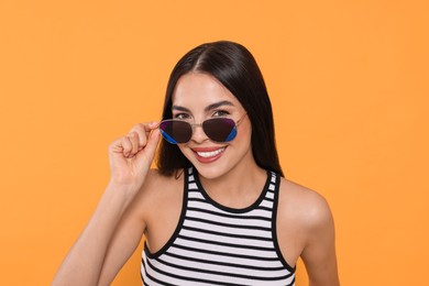 Attractive happy woman touching fashionable sunglasses against orange background