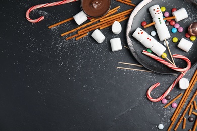 Flat lay composition with funny snowmen made of marshmallows on black table. Space for text