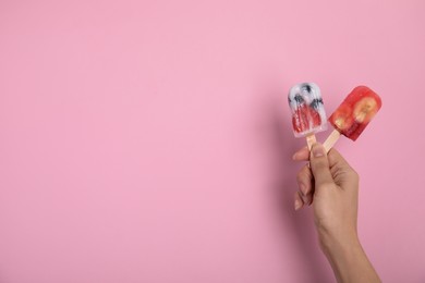 Photo of Woman holding berry popsicles on pink background, closeup. Space for text