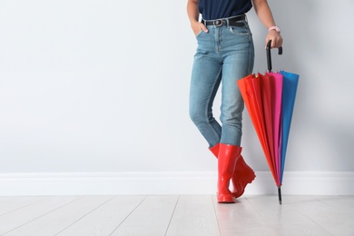 Woman in gumboots holding bright umbrella near white wall with space for design