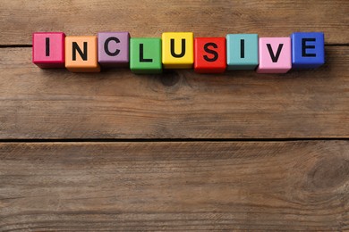 Photo of Colorful cubes with word Inclusive on wooden table, flat lay. Space for text