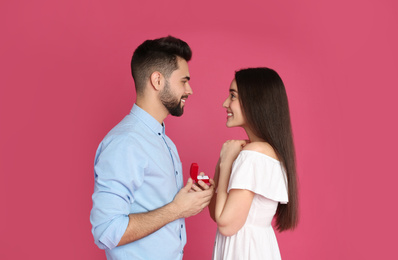 Man with engagement ring making marriage proposal to girlfriend on crimson background