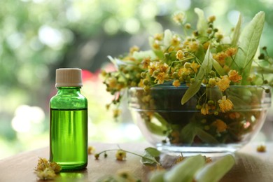 Photo of Bottle of essential oil and linden blossoms on wooden table against blurred background