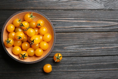 Ripe yellow tomatoes in bowl on dark wooden table, flat lay. Space for text