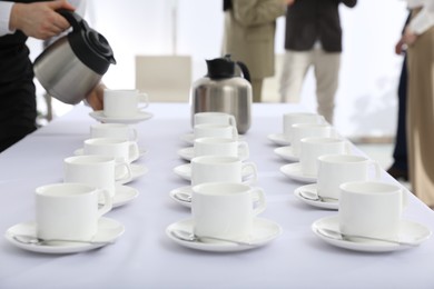 Photo of Waitress pouring hot drink during coffee break, focus on table with cups