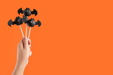 Woman with delicious bat shaped cake pops and space for text on orange background, closeup. Halloween celebration