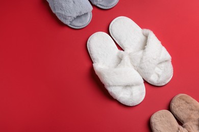 Different soft fluffy slippers on red background, flat lay. Space for text